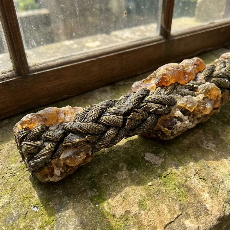 A braided golden rope studded with amber crystals resting on a weathered stone windowsill