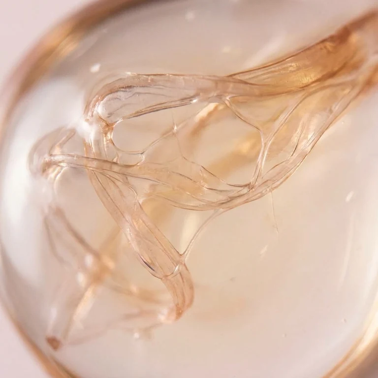 Un remolino de líquido ámbar translucido moviendose en espiral dentro de un recipiente de vidrio, iluminado con luz cálida